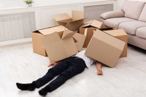Man met zwarte broek en wit shirt ligt onder een aantal kartonnen dozen
