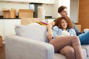 Couple sitting on couch with cardboard boxes behind them